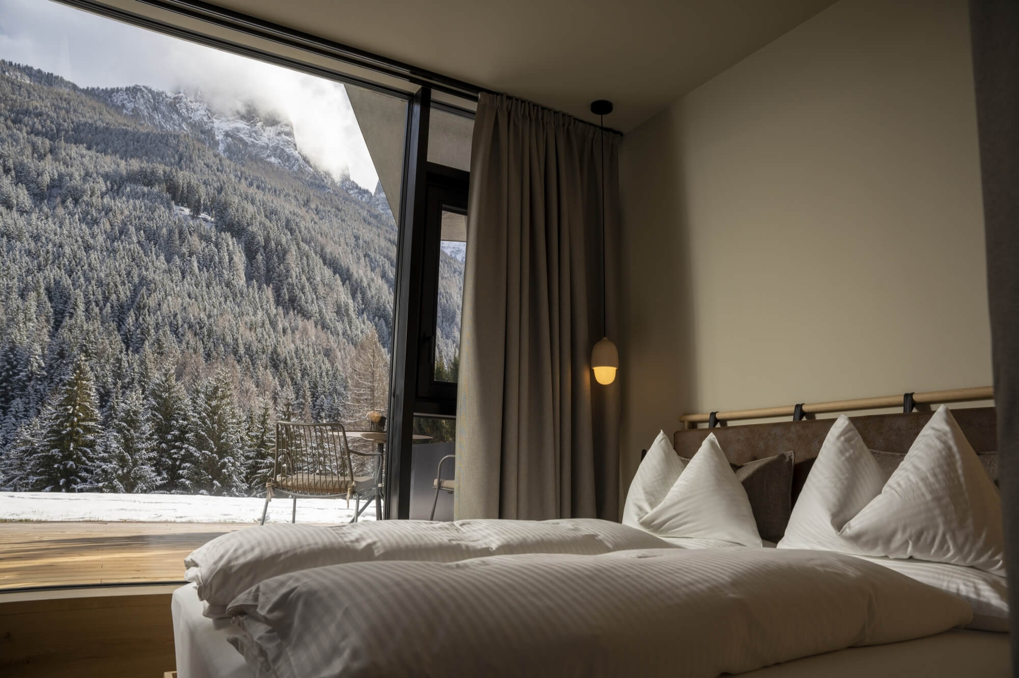 Camera d'hotel serena con vista sulle montagne, letto bianco, tavolo e sedie, atmosfera tranquilla e rilassante.