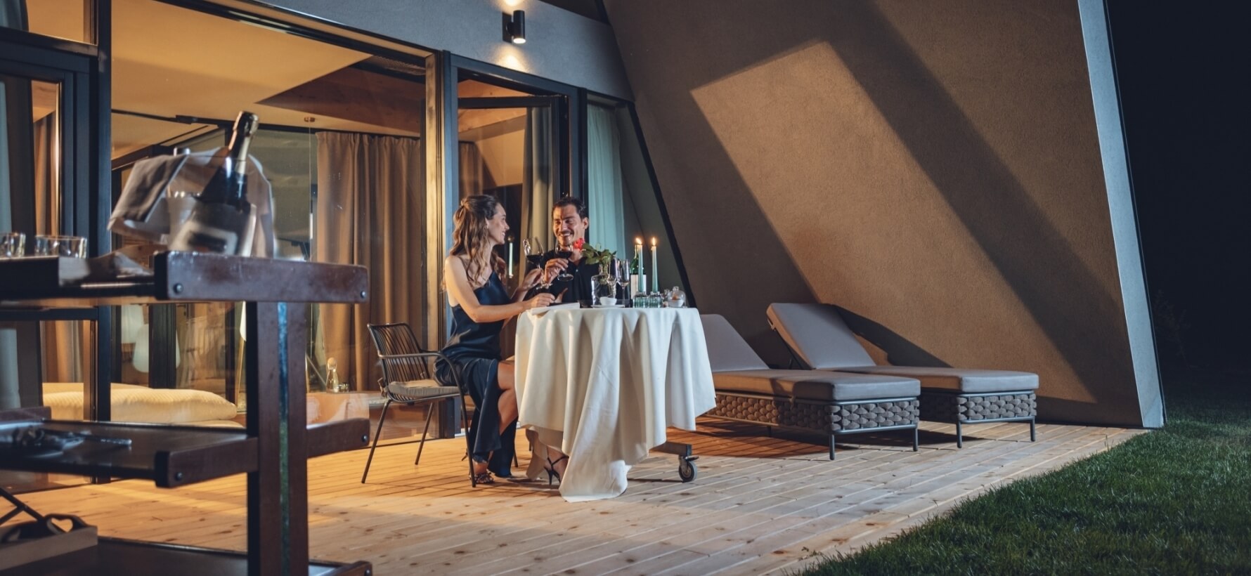 Cena romantica su un deck con uomo e donna, tavolo elegante, vino, candele e atmosfera intima.