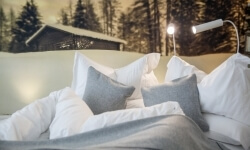 Letto con biancheria bianca, paesaggio invernale e lampada a muro.