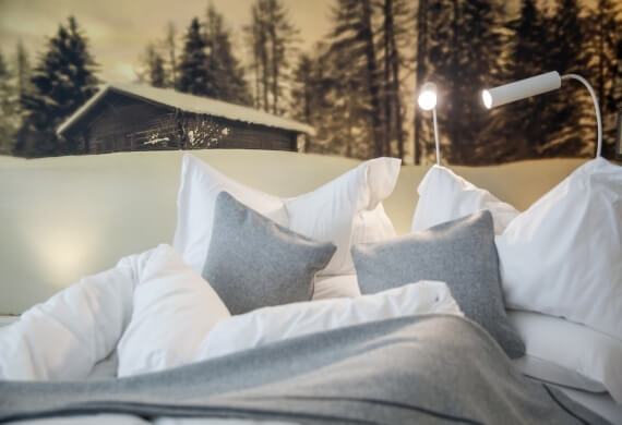 Letto con biancheria bianca, coperte grigie e murale di foresta.