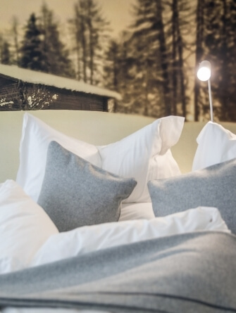 Letto con biancheria bianca, cuscini grigi e murale invernale.