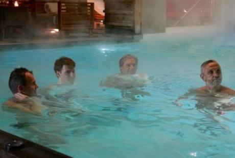 Uomini in una vasca idromassaggio, ognuno con diverse acconciature, in un'atmosfera rilassata e sociale.