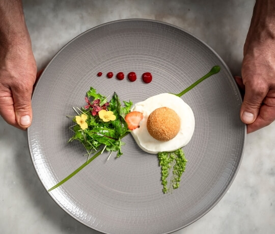 Piatto grigio con salsa bianca, fritto, purè verde e fiori.