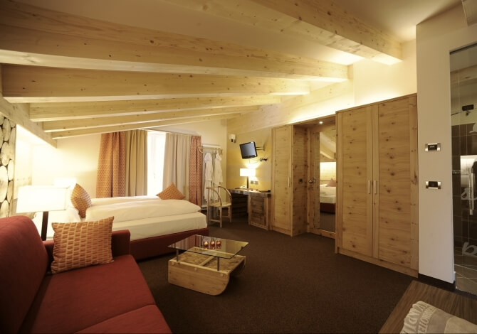 Camera spaziosa e moderna con letto, divano rosso, armadio in legno, scrivania e luce naturale, decorata in toni neutri.