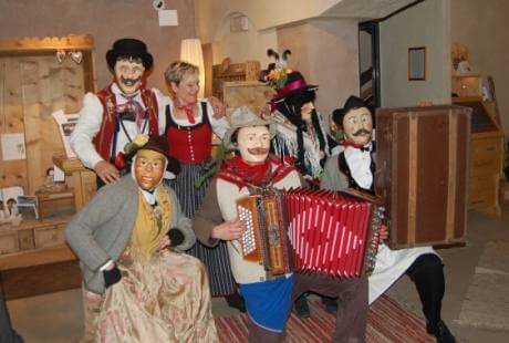 Gruppo di persone in abiti tradizionali tedeschi, con due musicisti che suonano l'accordeon in un ambiente accogliente.