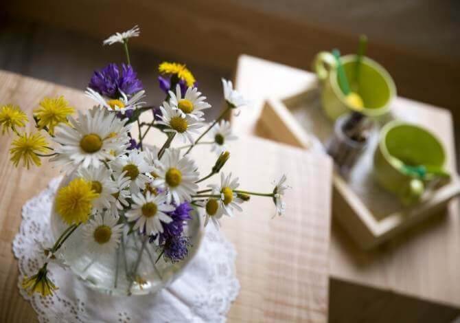 Vaso di fiori selvatici con mug su un vassoio, su un tavolo di legno chiaro, evocando un'atmosfera di calma.
