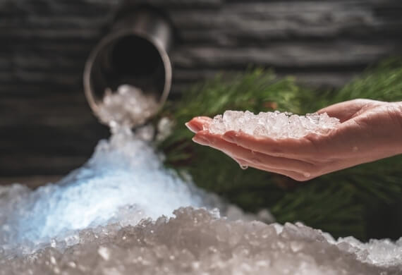 Una mano tiene ghiaccio tritato con un contenitore metallico sullo sfondo.