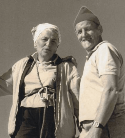 Foto in bianco e nero di una coppia anziana, uomo e donna, in abbigliamento semplice su sfondo grigio.