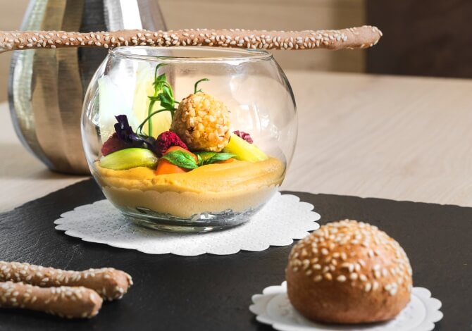 Ciotola di vetro con frutta e verdura, accompagnata da un grissino, su un centrino bianco su superficie nera.