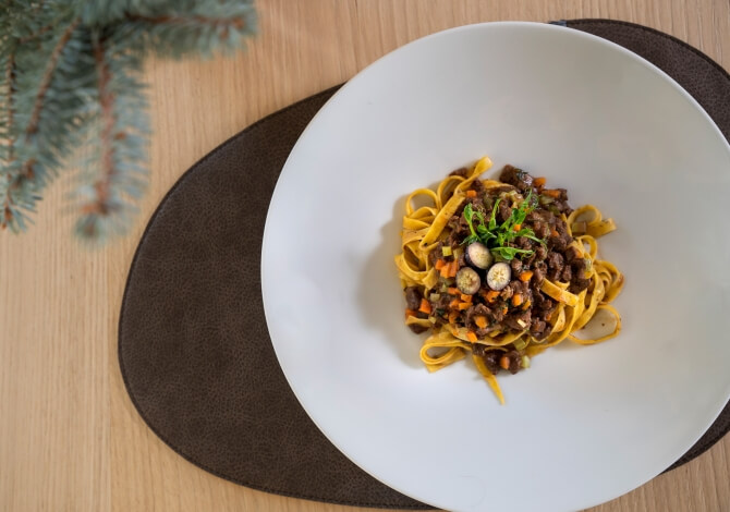Piatto bianco con pasta e salsa di carne, carote e funghi, decorato con erbe, su un tavolo di legno.