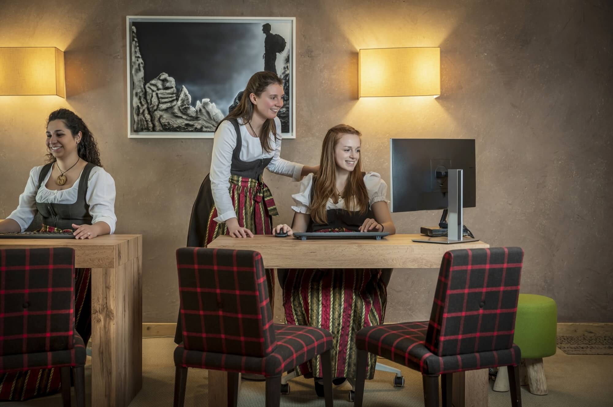 Tre donne in abiti tradizionali interagiscono con computer in un ambiente di lavoro professionale.