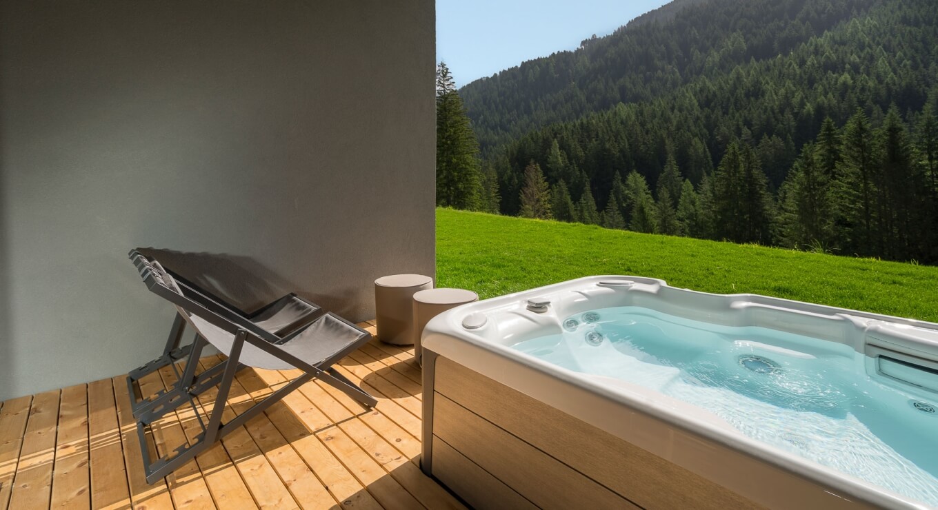 Vasca idromassaggio bianca su terrazza di legno con sedie grigie.