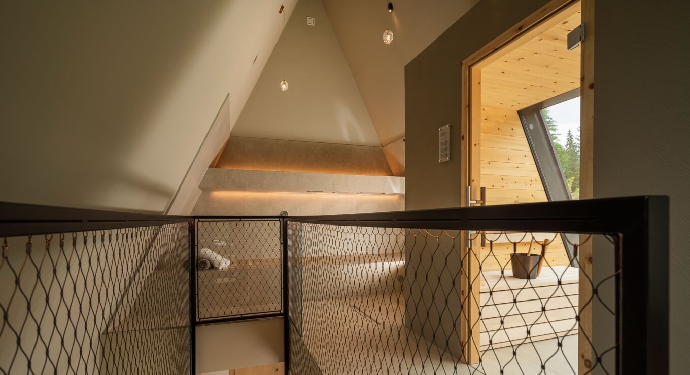 Interno di una casa moderna con scala, ringhiera nera, porta aperta verso l'esterno e pareti grigie e bianche.