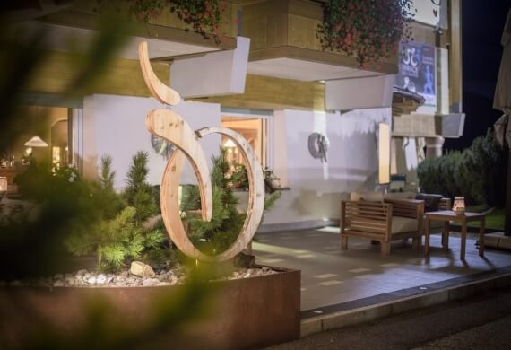 Scultura in legno a forma di bicicletta in un ambiente sereno, con un edificio bianco e un cartello blu sullo sfondo.