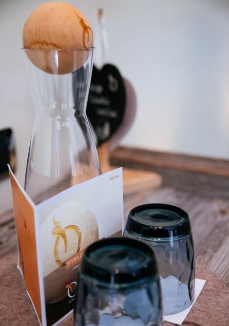 Caraffa di vetro con una sfera di legno e tre bicchieri vuoti su un tovagliolo bianco, sfondo sfocato.