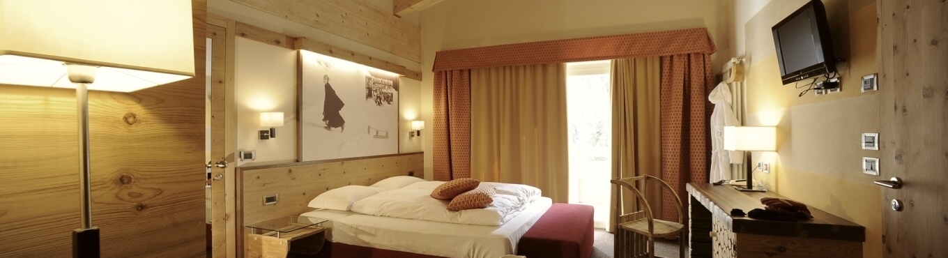 Camera d'hotel in legno naturale, letto king-size con lenzuola bianche, lampade e foto sopra la testiera.