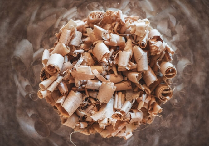 Primo piano di un mucchio di trucioli di legno marroni, con uno sfondo sfocato di forme simili a foglie.