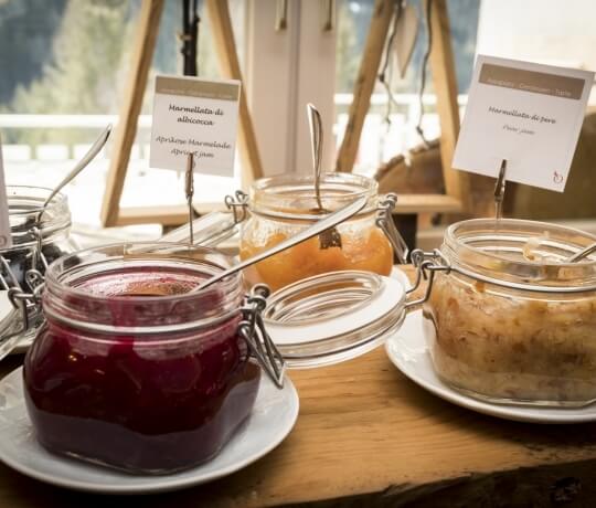 Collezione di barattoli di marmellata su un tavolo di legno, con etichette in lingua straniera e cucchiai.