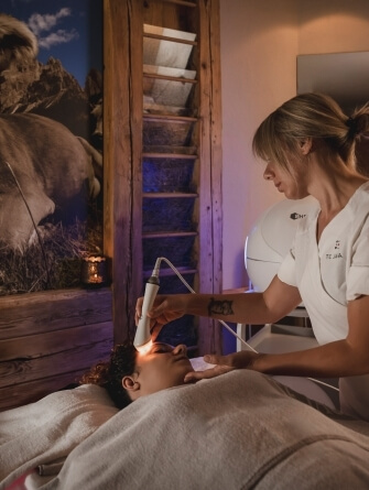 Una donna riceve un trattamento facciale in una spa, mentre un terapista utilizza un dispositivo luminoso.