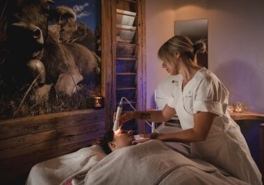 Una donna riceve un trattamento facciale in un ambiente sereno, mentre un'estetista la assiste con un dispositivo luminoso.