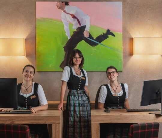Un gruppo di tre donne in abbigliamento coordinato, in un'area reception con un grande dipinto sullo sfondo.