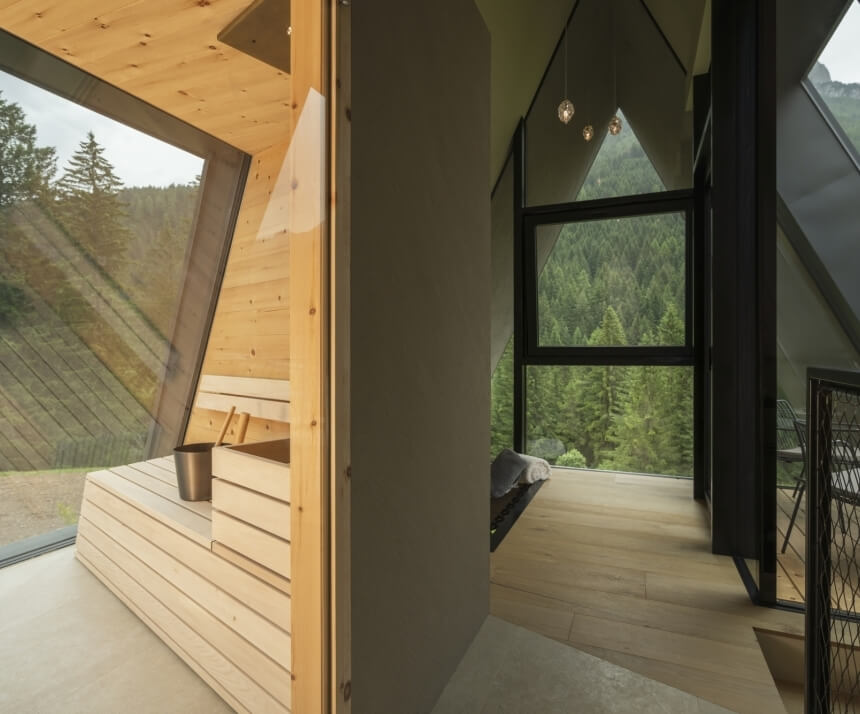 Cabina A-frame moderna con interni in legno chiaro e vista panoramica sulla foresta attraverso ampie finestre.
