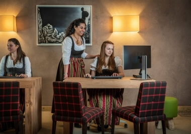 Tre donne in abiti tradizionali lavorano a scrivanie con computer.