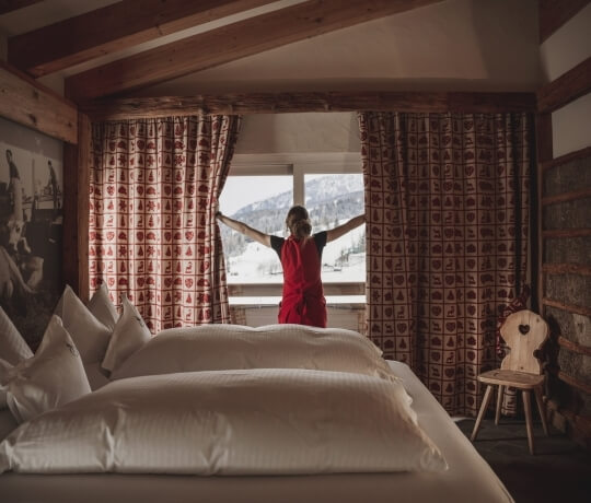Una donna in un hotel guarda il paesaggio invernale da una finestra, circondata da un'atmosfera accogliente e calda.