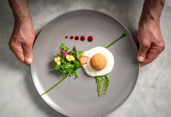 Piatto rotondo con sfera impanata, insalata e salse decorative.