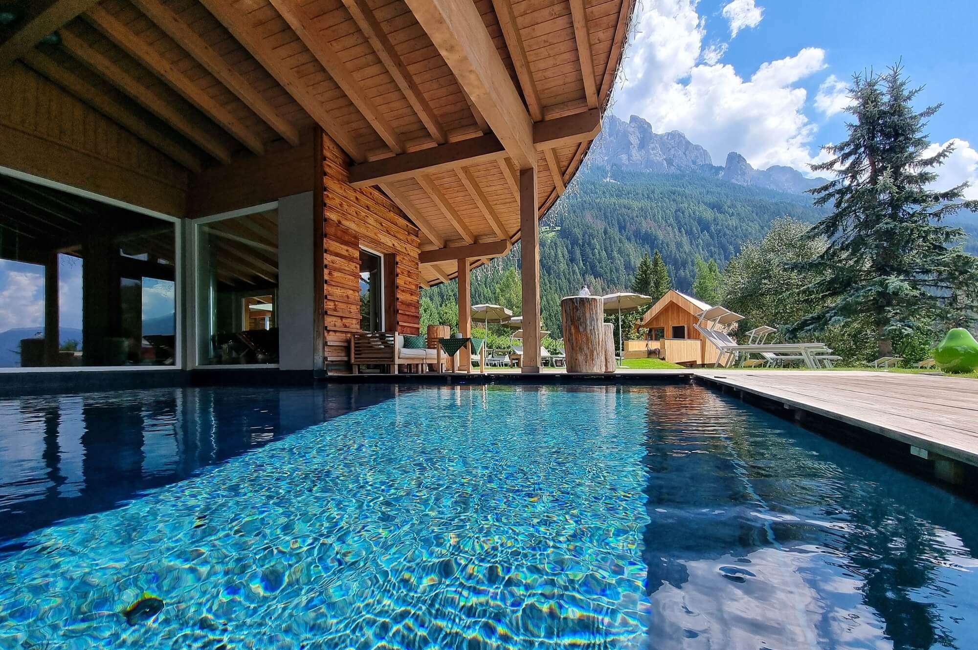 Immagine di un tranquillo rifugio all'aperto con piscina, una cabina in legno e montagne sullo sfondo.