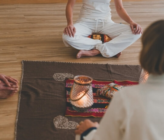 Due persone sedute su un pavimento di legno con cuscini e una lanterna.