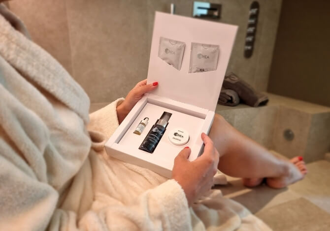 Una donna in accappatoio bianco tiene una scatola aperta con prodotti per la cura della pelle in un bagno elegante.