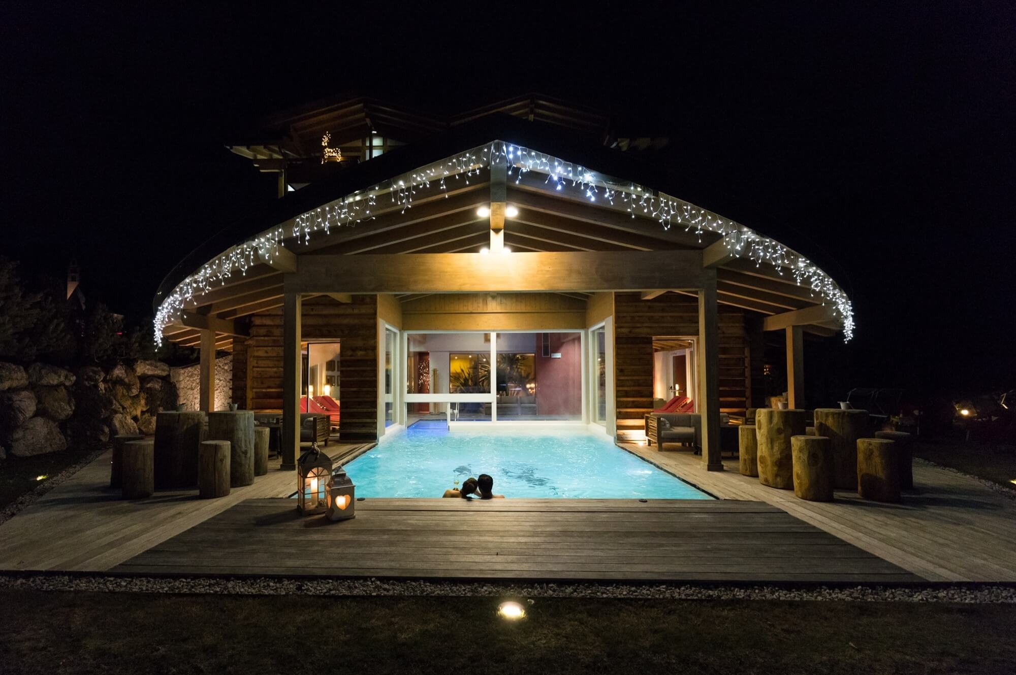 Una serena scena notturna con una casa piscina illuminata da luci a stringa e una vista accogliente dell'interno.