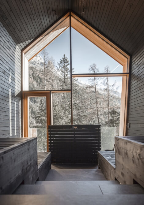 Una stanza con un grande finestra triangolare, pavimento grigio e vista su alberi, trasmette serenità e tranquillità.