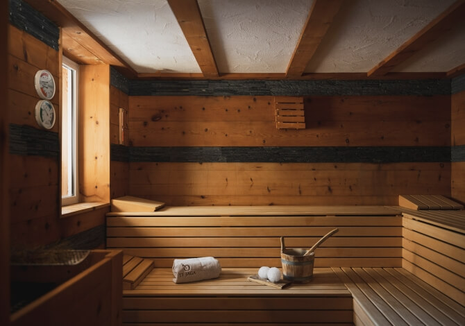 Interno di una sauna con pareti in legno, panca, asciugamani arrotolati e luce naturale che entra da una finestra.