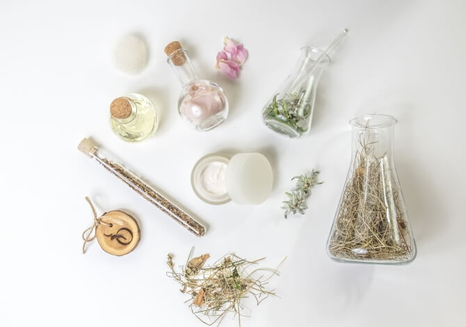 Disposizione di contenitori di vetro, erbe secche e oggetti bianchi su una superficie bianca, evocando creatività e armonia.