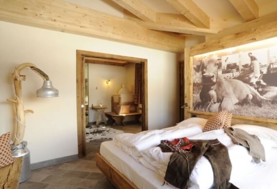 Camera rustica con letto grande, pittura di maiali, lampada in legno e porta che conduce a un bagno.