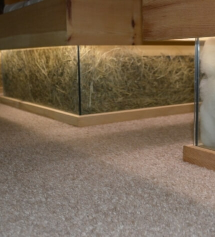 Piattaforma in legno con vetrina in vetro riempita di fieno e oggetto bianco avvolto in plastica a destra.