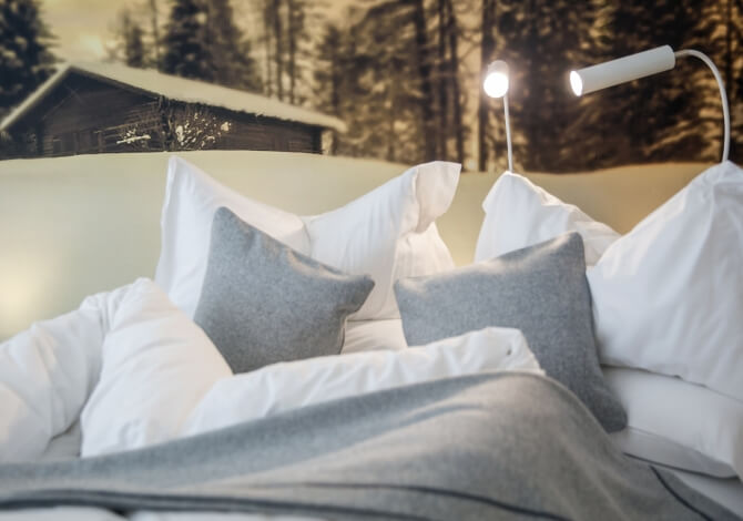 Letto con cuscini bianchi, coperta grigia e arte murale innevata.