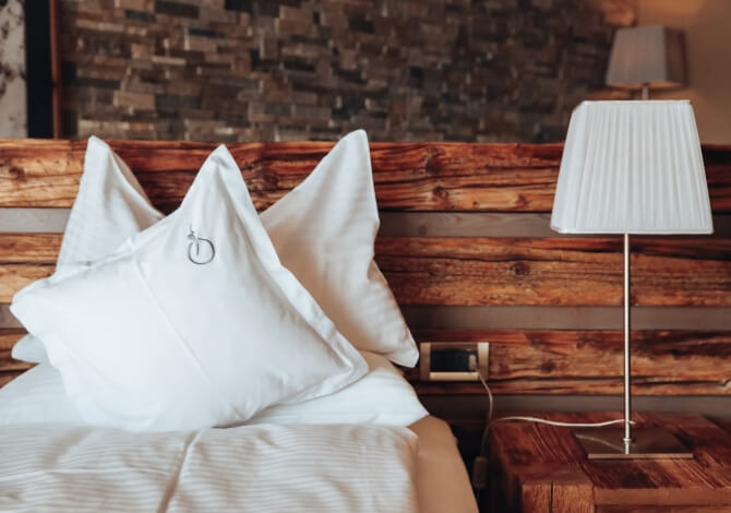 Camera d'hotel accogliente con letto, comodino, lampada e carta da parati in legno scuro.