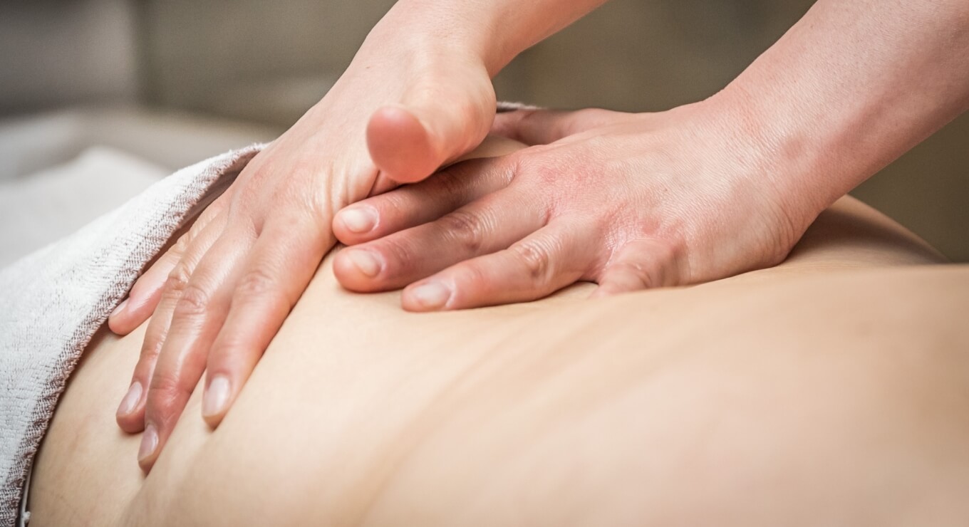 Una persona riceve un massaggio, con il terapista che lavora sulla schiena del cliente sdraiato su un tavolo da massaggio.