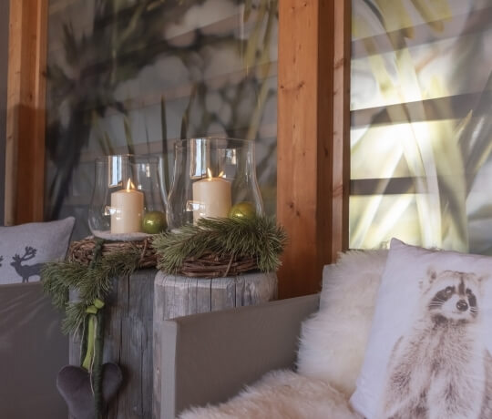 Una scena invernale accogliente con un divano bianco, candele in un vaso di vetro e una finestra con tende bianche.