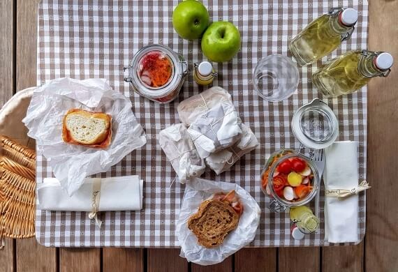 Un picnic su una tovaglia a scacchi con panini, mele, succhi, verdure sott'aceto e posate su un tavolo di legno.