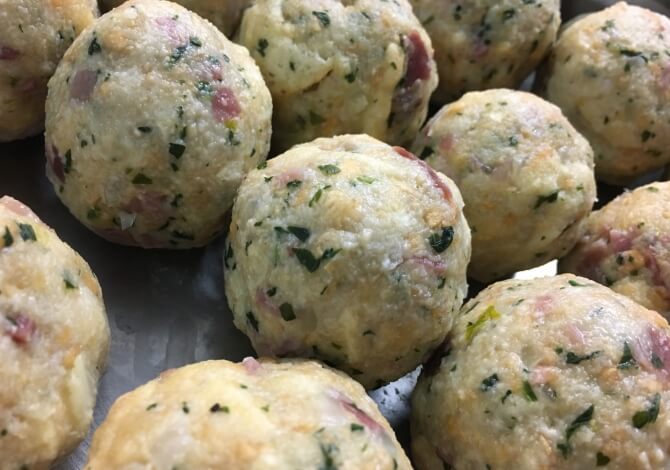 Primo piano di palline chiare con macchie scure, su una superficie metallica, suggerendo preparazione culinaria.