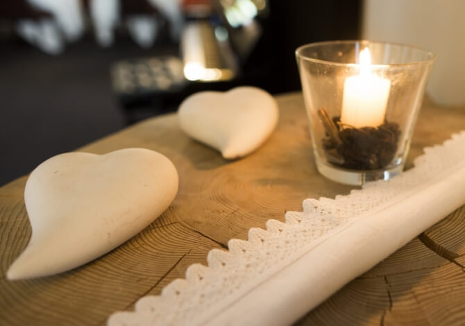 Candelabro con candela accesa e cuori bianchi su un tavolo di legno, decorato con un runner di pizzo bianco.