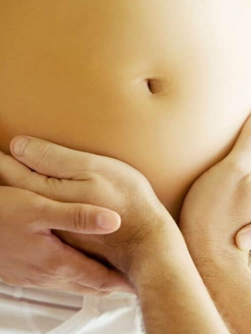 Due mani sostengono un pancione di gravidanza, sfondo sfocato.