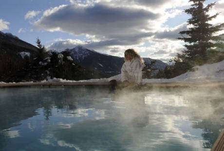 Una donna in accappatoio bianco siede accanto a una piscina circondata da un paesaggio innevato e montagne maestose.