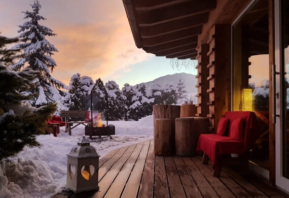 "Cabina invernale accogliente con lanterna a forma di cuore, camino e panorama montuoso innevato."