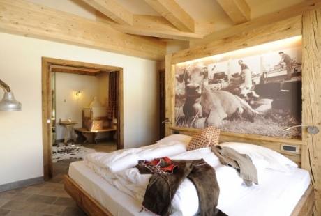 Camera d'albergo elegante con letto matrimoniale, cucina moderna, pareti bianche e travi in legno a vista.