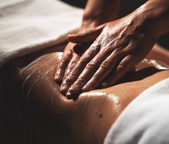 Mani massaggiano una schiena unta d'olio, con asciugamani bianchi.